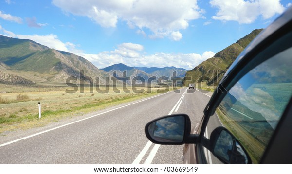 Driving view from\
side of car mirror mountain valley. Beautiful landscape of a road\
in the mountains on sunny\
day