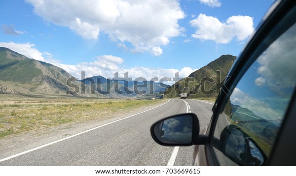 Driving view from side of car mirror mountain\
gorgeous valley. Beautiful landscape of a road in the mountains on\
sunny day.