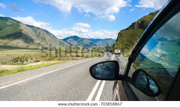 Driving view\
from side of car mirror mountain valley. Beautiful landscape of a\
road in the mountains on a sunny\
day