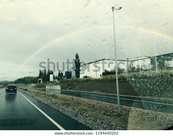 Drizzle on the windshield while driving in rain.\
Wet road and rainbow in the\
sky