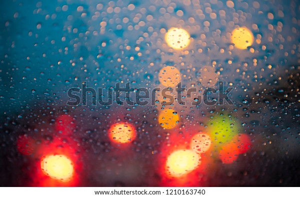 Drizzle rain drop on glass with street colorful\
traffic lights at night blur bokeh abstract background. Raining\
season concept