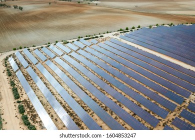 Drone Aerial Shooting Of Solar Power Farm Raws Of Reflective Panels. At Cloudy Day In Spain.