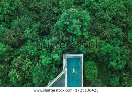 Drone aerial shot of woman relaxing in awesome infinity swimming pool hiding in jungle, Bali. Travel concept, luxury vacations in Asia, summer holidays.
