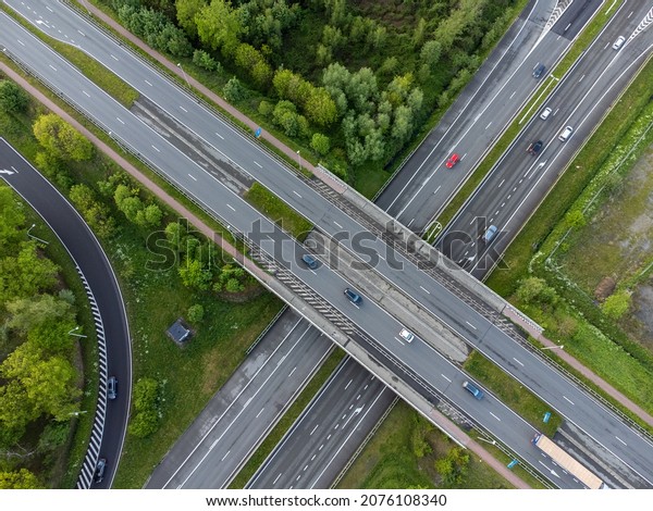 Drone aerial top down shot of cars and traffic\
driving on the motorway surrounded by green grass and trees. View\
from above