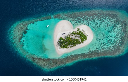 Drohne Luftaufnahme einer schönen tropischen, herzförmigen Insel unter blauem Meerwasser im Paradies der Malediven mit Schiff auf Hintergrund