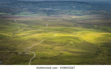 Drone or aerial view on winding wooden path and boardwalk between green fields illuminated by sunlight in Cuilcagh Mountain Park, Northern Ireland - Powered by Shutterstock