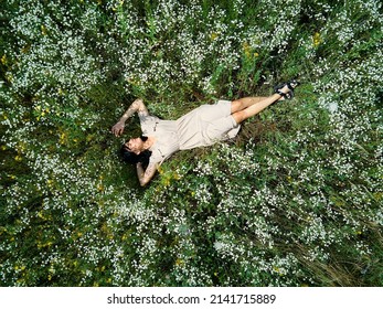 Drone Aerial View Of Relax Woman In Dress Lying On Flower Blooming Meadow, In Countryside, In The Field On Summer Day, Feel The Nature, Alone Travel. Slow Motion, Top View.