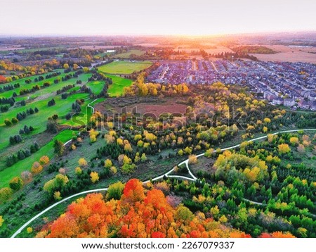 Drone aerial view of suburban residential neighborhood houses surrounded by beautiful autumn fall color, park, trails, nature greenbelt under golden sunset. Development, housing, real estate cityscape