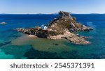 Drone aerial view of white and blue small church in an island in front of Agios Stefanos Beach in Kos Greece