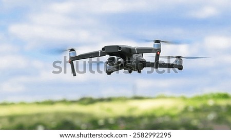 Drone with a camera flies against the background of trees and sky. An unmanned flying object. The drone hovers in the air and is used for terrain surveillance and video filming