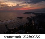 Drone capture of coastal cityscape at dusk with vibrant sunset sky. Urban shoreline illuminated as day transitions to night. Ocean view on sunset. Sunrise above sea. Mirissa, Sri Lanka. Aerial.