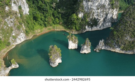 Drone capture of an emerald green lake surrounded by steep limestone cliffs and lush forests, with isolated rock formations emerging from the water. - Powered by Shutterstock