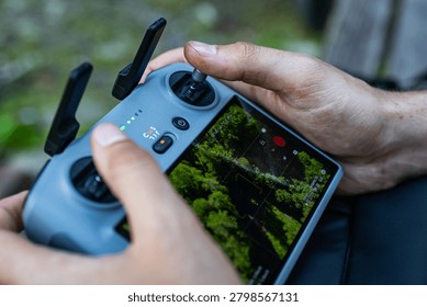 Drone controller screen displays a bright forest scene with focus aids and telemetry. The operator holds the device steadily while planning a clean aerial route above the summer canopy