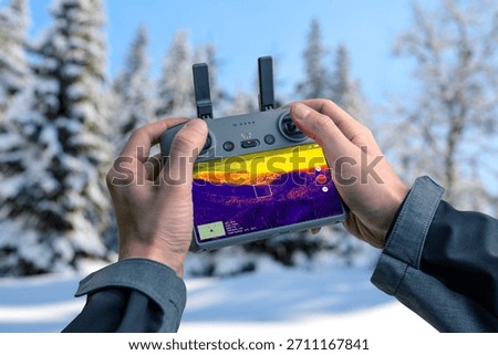 Drone controller with thermal imaging overlay used for search and rescue operations, highlighting heat signatures across forest terrain for emergency detection and safety missions