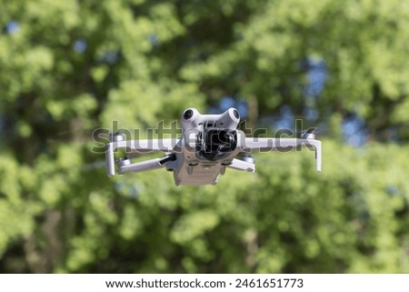 Drone device with digital camera flying in air against green foliage in sunny day. Outdoor activity with quadcopter.