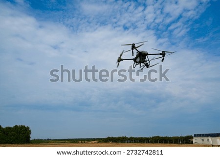 Drone in flight over open fields on a clear day with a distant farm building