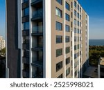 A drone flyby showcasing a modern high-rise building with sleek balconies and large windows. The ocean and surrounding greenery in the background enhance the urban-coastal appeal