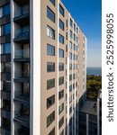 A drone flyby showcasing a modern high-rise building with sleek balconies and large windows. The ocean and surrounding greenery in the background enhance the urban-coastal appeal