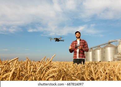 Drone hovers in front of farmer with remote controller near grain elevator. Quad copter flies near pilot. Agronomist taking aerial photos and videos in a wheat field. Innovations in agriculture.