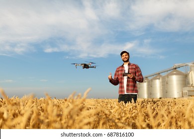 Drone Hovers In Front Of Farmer With Remote Controller Near Grain Elevator. Quad Copter Flies Near Pilot. Agronomist Taking Aerial Photos And Videos In A Wheat Field. Innovations In Agriculture.