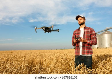 Drone Hovers In Front Of Farmer With Remote Controller Near Grain Elevator. Quad Copter Flies Near Pilot. Agronomist Taking Aerial Photos And Videos In A Wheat Field. Innovations In Agriculture.