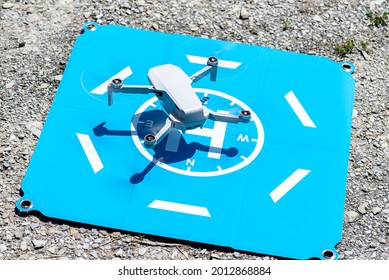 The Drone Hovers Over The Blue Landing Pad On The Rocks, The Plastic Propellers Are On, A Visible USB Slot And A Memory Card.