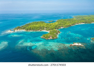 Drone image capturing Islas del Rosario in Cartagena, Colombia, surrounded by turquoise Caribbean waters, visible coral reefs, tropical trees, and several boats anchored close to the island.