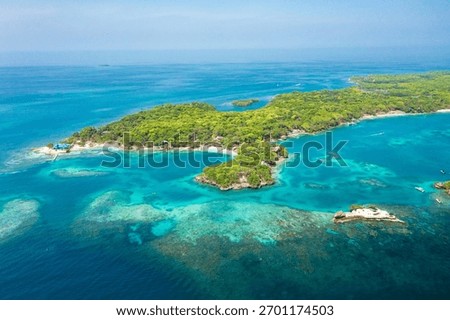 Drone image capturing Islas del Rosario in Cartagena, Colombia, surrounded by turquoise Caribbean waters, visible coral reefs, tropical trees, and several boats anchored close to the island.