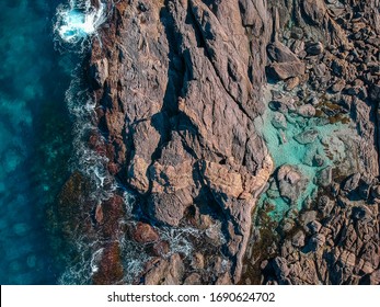 A drone image of a person flaoting in a calm and safe, turquoise coloured rockpool with the ocean crashing just over the natural break wall.