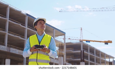 Drone operator holding remote controller. Professional builder in helmet and vest standing in front of construction site. Office building and crane background. Business, real estate and investment. - Powered by Shutterstock - Get 15% off with code: PIKWIZARD15