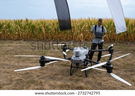 Drone operator tests aerial drone in a cornfield with banners and equipment in open field