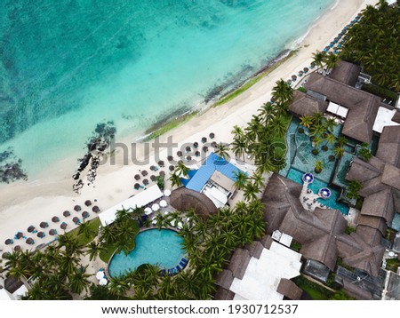 Drone overhead view of the front  beach of Constance Belle Mare Plage, with pools, garden, palm trees, umbrellas and a beautiful turquoise sea with transparent water. Luxury 5 star hotel in Mauritius.