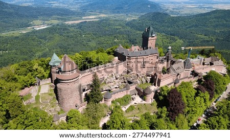 Drone perspective capturing the full extent of Haut-Koenigsbourg fortress, showcasing its stone walls, multiple towers, and imposing presence on a forested Alsace ridge.