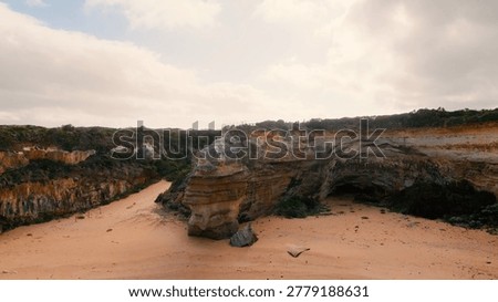 Drone perspective of rugged limestone cliffs and a sandy beach under a cloudy sky.