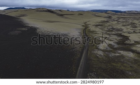 Drone perspective of single-lane road bisecting dark volcanic lava field and moss-covered ground in Skaft?rhreppur region, southeastern.