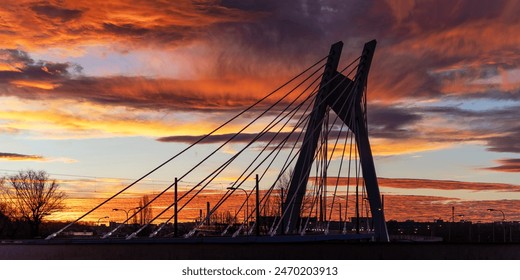 Drone perspective view of suspension bridge silhouette and skyline of Krakow, Poland. Aerial panoramic photo of modern bridge structure in dramatic dark sunset sky with fluffy colorful clouds - Powered by Shutterstock