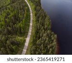 Drone photo of curvy road with forest around it. Finland majestic nature. Sunny early summer day. Birds eye view of the Finland