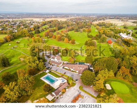 Drone photo of golf course including green, club house, trees, during the fall season.