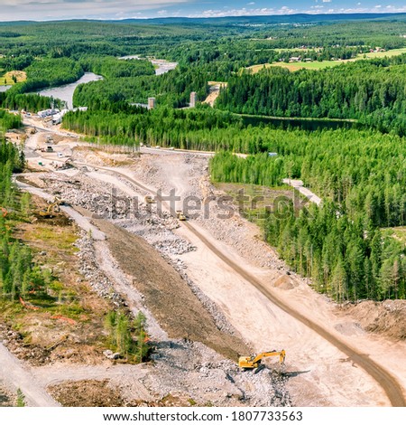Drone photo on construction of new highway and bridge over Umea river - many heavy industrial machines work together - dump trucks, bulldozer and excavator. High altitude overview on construction site