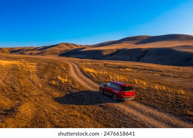 Drone photo red SUV driving on a winding dirt and rocks paved road through a rolling hill landscape at sunset in Gareji area in Georgia. The travels towards the horizon, creating a sense of adventure. - Powered by Shutterstock