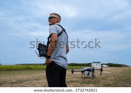 Drone pilot with controller stands in field preparing quadcopter for takeoff outdoors