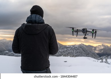 Drone Pilot Flying UAV Over Snowy Mountains At Sunrise