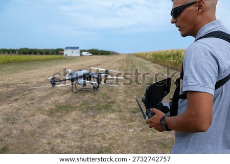 Drone pilot operates handheld controller in open field with drone ready to fly