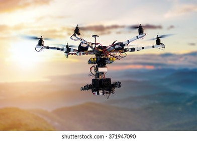 The drone with the professional cinema camera flying over the misty mountains at sunset. Blurred background. Innovation photography concept. Heavy lift drone photographing city at sunset. 