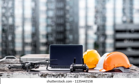 Drone, remote control, laptop computer and protective helmet at construction site. Using unmanned aerial vehicle (UAV) for land and building site survey in civil engineering project.