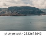 A drone scenic view of a mountain from the Scottish Highlands in the background of a lake with sailing boat on a cloudy day