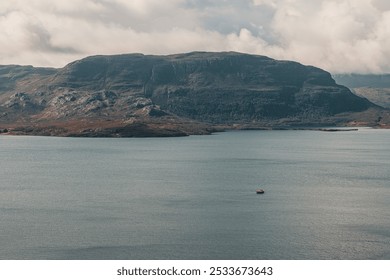 A drone scenic view of a mountain from the Scottish Highlands in the background of a lake with sailing boat on a cloudy day - Powered by Shutterstock