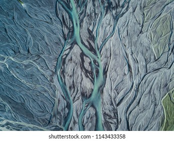A drone shot from above on a green and blue metallic looking glacier river stream in Iceland with repeating grey, beige and dark green patterns, textures and structures running from top to down
