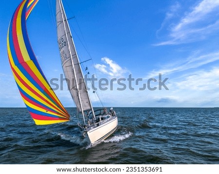 Drone shot of the bow of a sailboat healed over with a bright colourful genoa, gennaker, or asymmetric spinnaker headsail in windy conditions under blue sky in The Netherlands