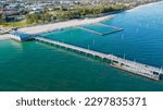 A drone shot of the Busselton Jetty on the sandy beach and the coastal buildings in Busselton, Australia